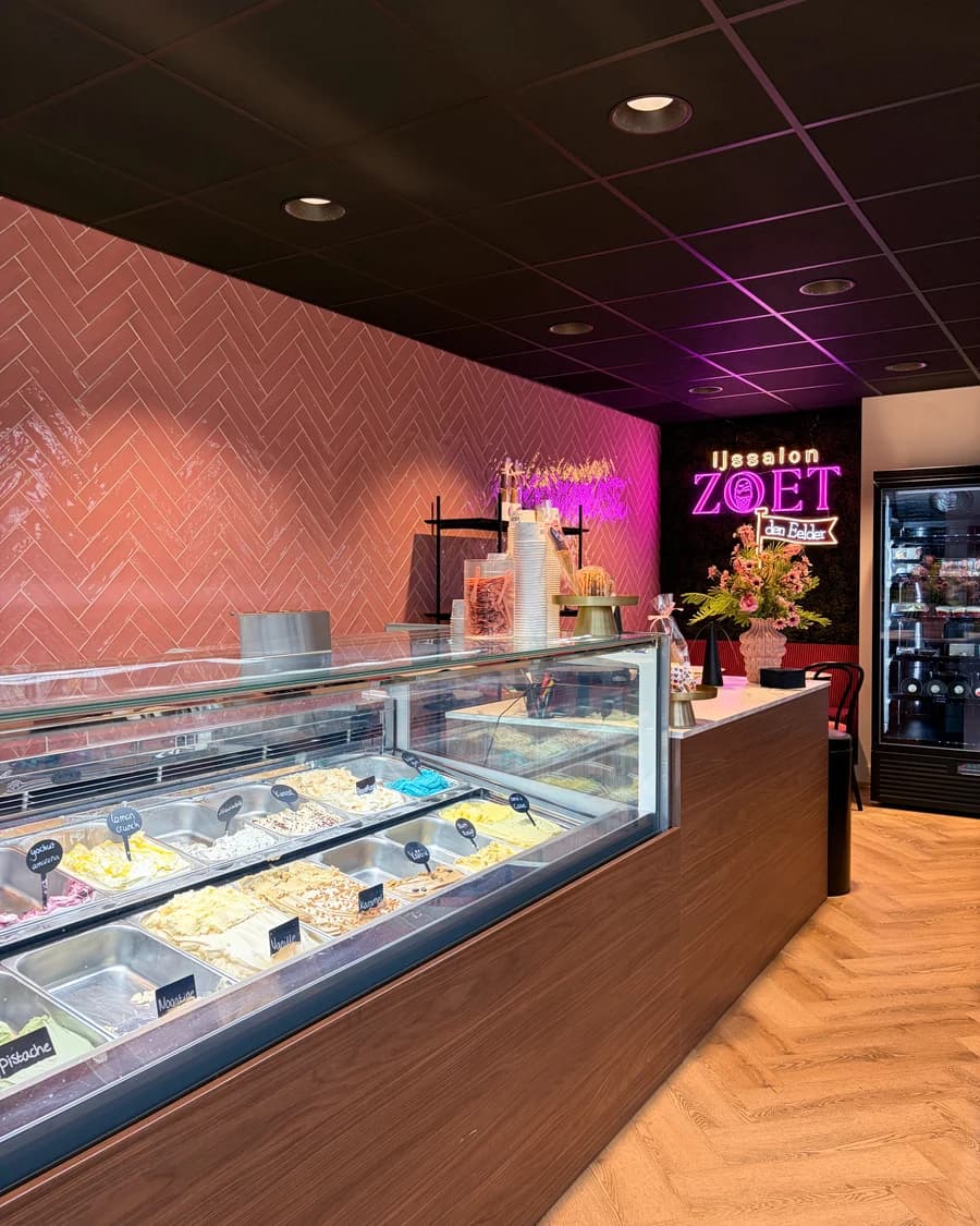 De ijsvitrine met de smaken van de dag, met de roze tegelwand en het neonlogo erachter